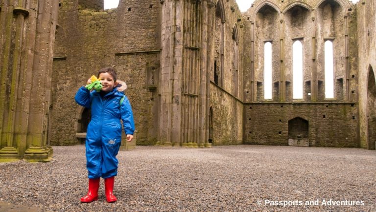 The Rock Of Cashel With Kids - Boy in blue rainsuit holding a green dragon in the Abbey.