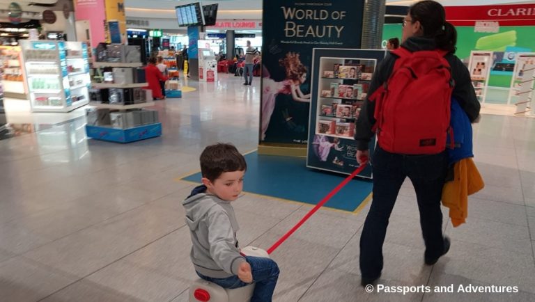 Awesome Tips For Flying With Babies and Toddlers - A mu pulling her son on a jetkids bedbox through an airport