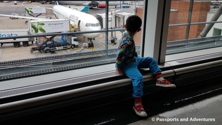 Awesome Tips For Flying With Babies and Toddlers - A toddler in pyjamas in an airport looking out the window at a plane