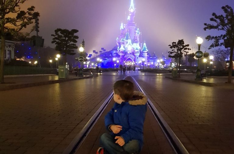 A young boy sat on the rail tracks in front of the Sleeping Beauty Castle at night in Disneyland Paris