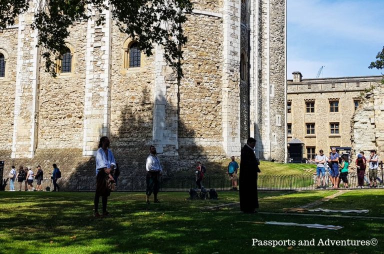 Three actors on the grass in front of the White Tower at the Tower of London acting out an event