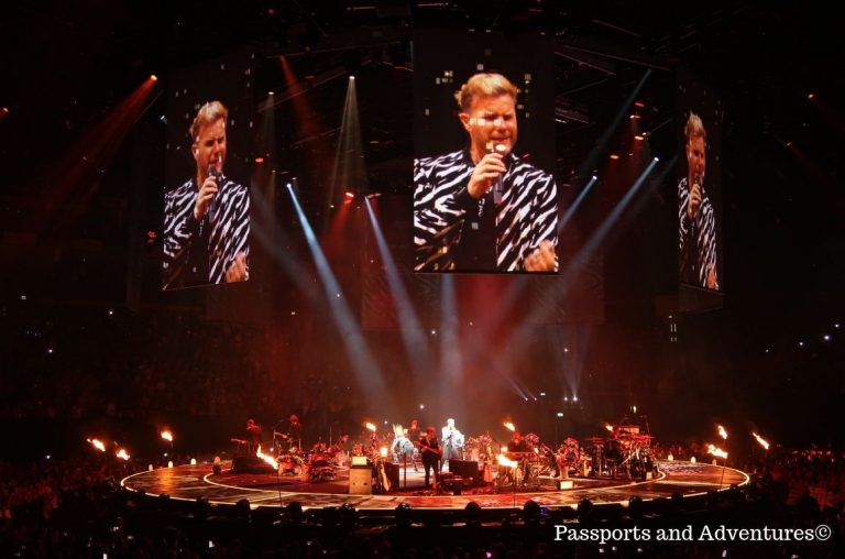 A picture of a stage in the O2 from a Take That concert with Gary Barlow on the screens overhead