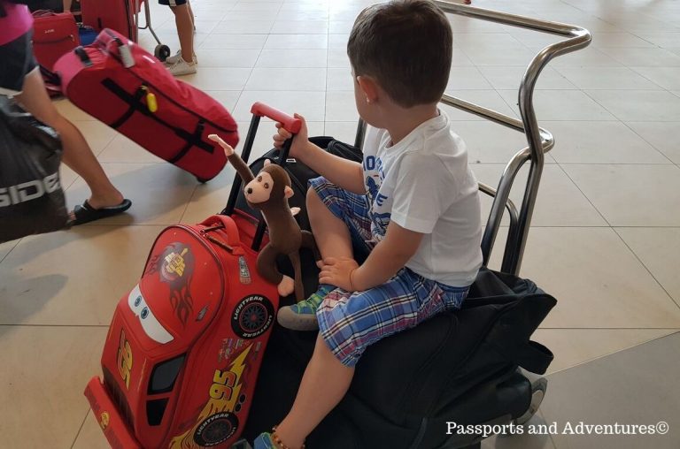 A little boy sitting on luggage on a luggage trolley in an airport