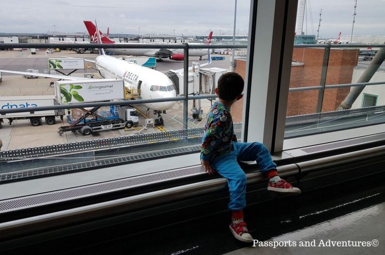 A little boy sitting at a window looking down at a Delta Airways plane in Heathrow airport