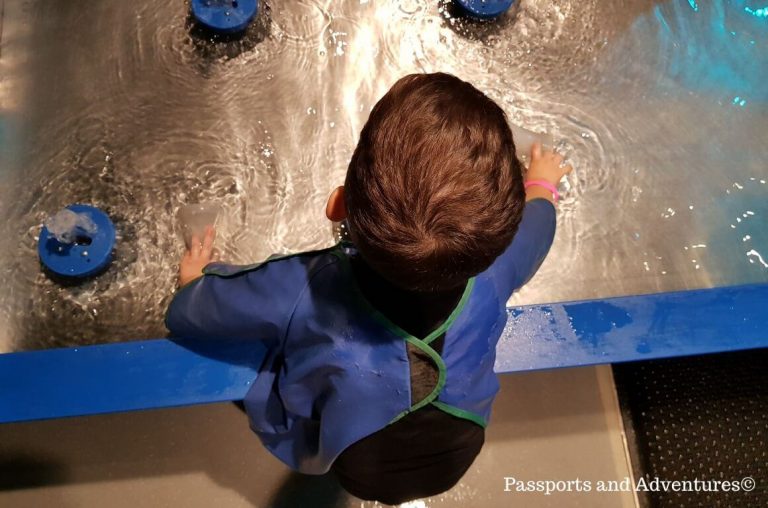 A young child in a blue apron playing at a water table in the Portland Science Museum