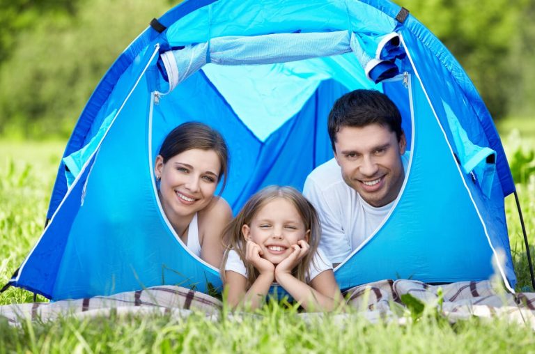 A family of three looking out from a blue tent in a green field of grass