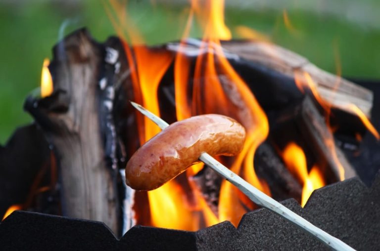 A sausage being cooking on a skewer over a campfire flame
