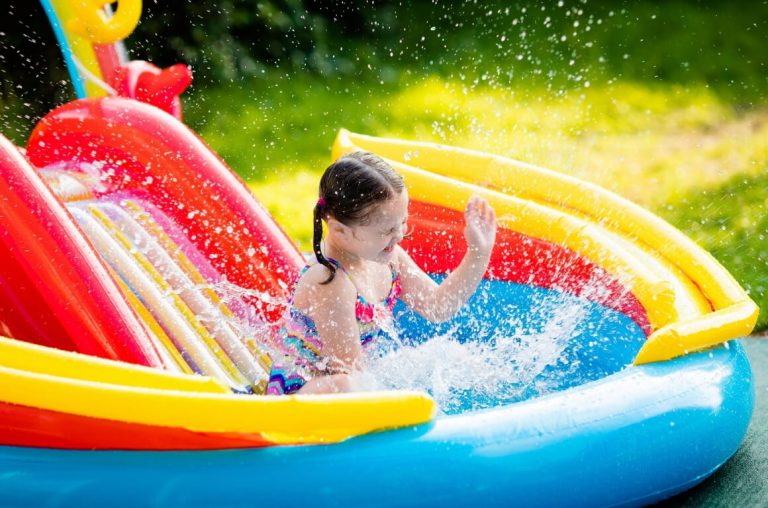 A young girl splashing water in an inflatable pool with a slide behind her