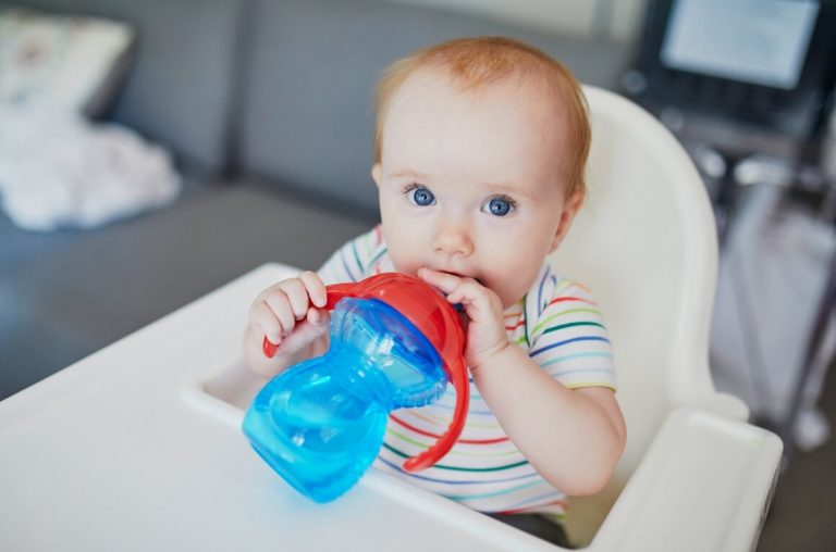 A picture of a baby in a high chair with a blue sippy cup